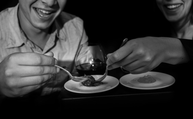 image en noir et blanc de deux personnes dégustant un repas dans le noir