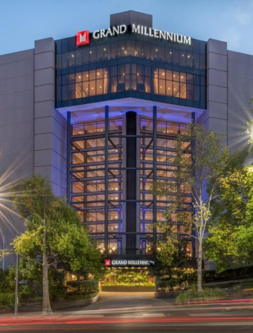 Exterior view of the Grand Millennium Auckland hotel at night, with illuminated windows and modern architecture surrounded by trees